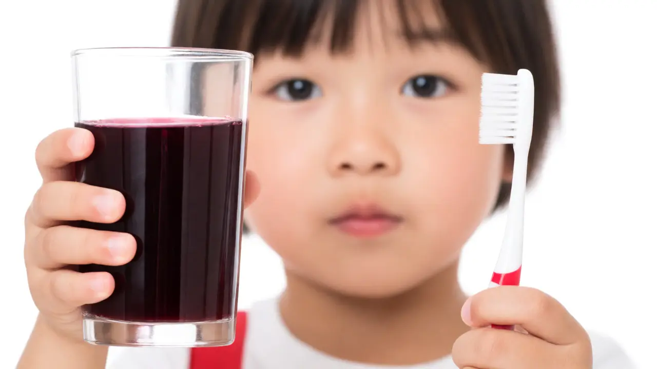Dítě drží sklenici tmavé šťávy a zubní kartáček jako prevenci zabarvení